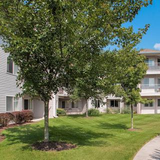 A view of an apartment complex with a well-maintained lawn and trees.