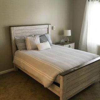 A cozy bedroom with a neatly made bed, bedside lamp, and window bringing in natural light.