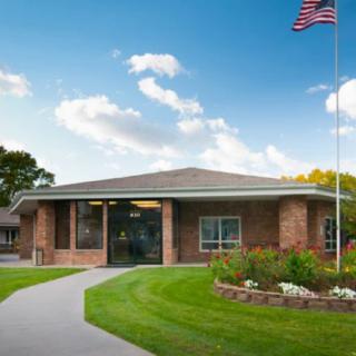 A brick building with an American flag and a well-maintained garden pathway under a partly cloudy sky.