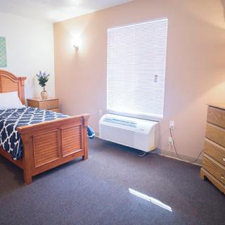 A cozy bedroom with a single bed, wooden furniture, and a window letting in natural light.