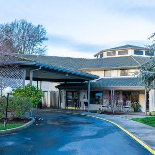 The photo shows the front entrance of a building with a covered driveway and landscaped surroundings.