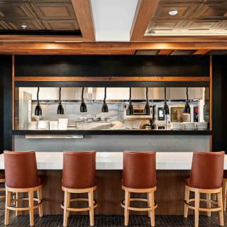 A modern restaurant interior with a view of the kitchen area and bar stools at the counter.