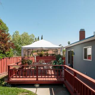 A cozy backyard deck with a canopy and outdoor seating, surrounded by a wooden fence on a sunny day.