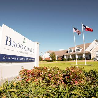 A senior living community facility with a welcoming sign and flags in the front.
