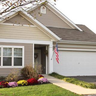 A charming suburban home with colorful flower beds and an American flag.