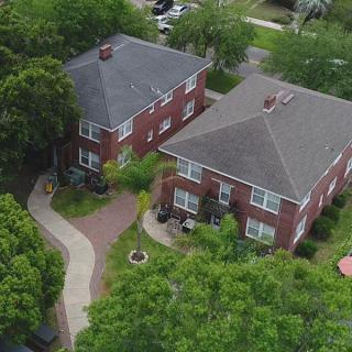 Aerial view of two brick houses surrounded by trees in a residential neighborhood.