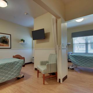 A hospital room with two beds, a wall-mounted TV, and a chair.