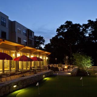 An outdoor restaurant patio lit up in the evening, surrounded by trees.
