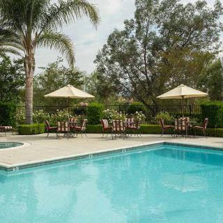 A tranquil outdoor pool area with seating and umbrellas surrounded by lush greenery.
