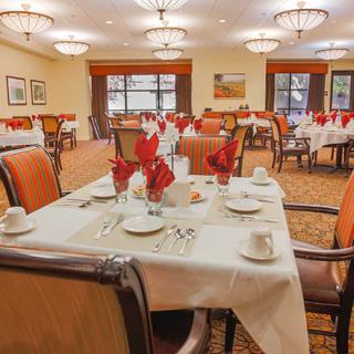 A neatly arranged dining room with elegant table settings, featuring red napkins and ambient lighting.