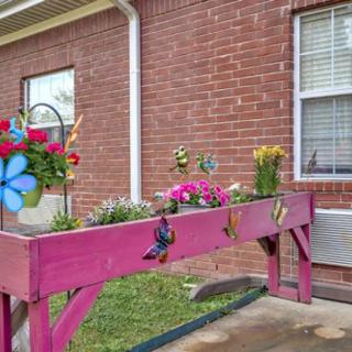 A vibrant pink elevated planter filled with colorful flowers against a brick wall backdrop.