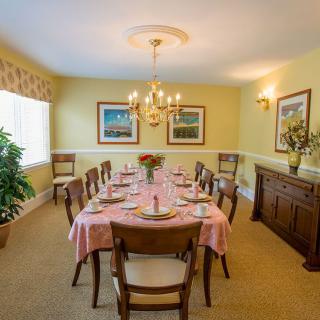 A cozy dining room with a large table set for a meal, featuring a chandelier and artwork on the walls.