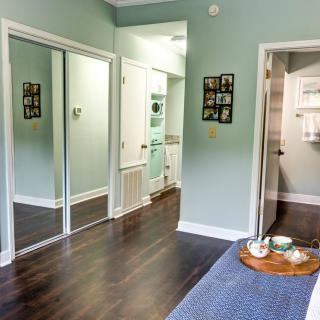 A well-lit bedroom with hardwood flooring, featuring a mirrored closet and a tray with glasses on the bed.