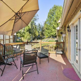 A sunny deck with outdoor furniture and an umbrella, surrounded by trees.