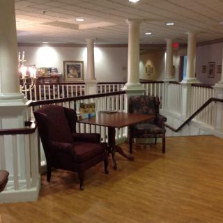 A cozy indoor seating area with chairs and a table on a wooden floor, surrounded by white railings and soft lighting.