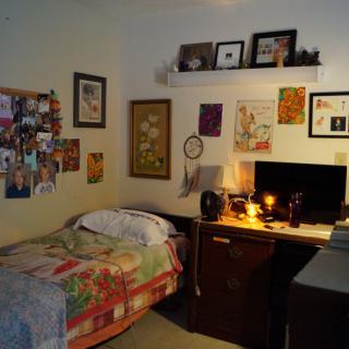 A cozy bedroom with a single bed, a decorated desk area, and personal touches on the walls.