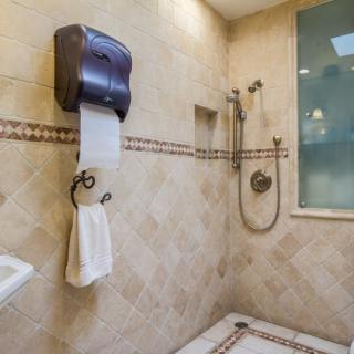 A well-designed bathroom featuring a spacious shower area, tiled walls, and amenities such as a towel holder and paper dispenser.