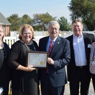 A group of people posing for a photo, with one person holding a certificate during an outdoor award ceremony.