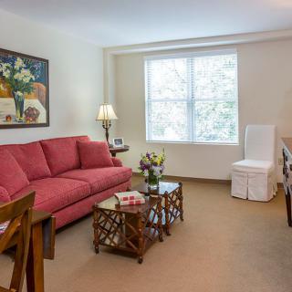 A cozy living room with a red sofa, art on the wall, and a well-lit window.