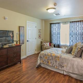A cozy and well-decorated bedroom with a bed, wooden dresser, and patterned curtains.