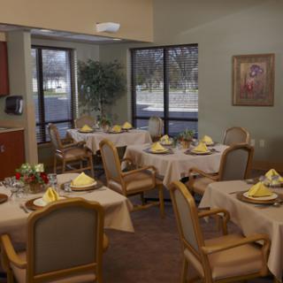 A well-furnished dining room set for a meal, featuring elegantly arranged tables with yellow napkins and a pleasant view outside.