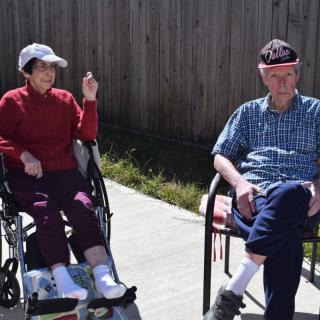 An elderly couple enjoying a sunny day outdoors, sitting together with one in a wheelchair.