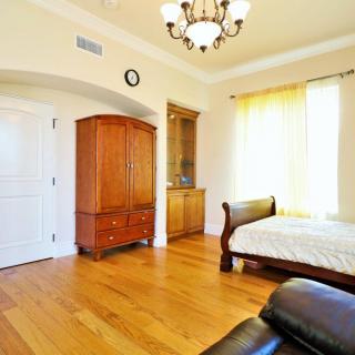 A spacious bedroom with wooden flooring, featuring a bed, wardrobe, and chandelier lighting.