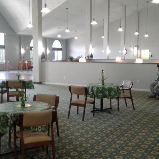 A modern and spacious interior with tables and chairs arranged in a carpeted area, illuminated by pendant lights.