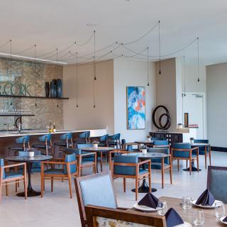 A modern restaurant interior with neatly arranged tables and chairs, featuring a bar and contemporary decor.