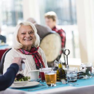An elderly woman smiling while enjoying a meal at a restaurant.