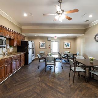 A cozy kitchen and dining area with wooden cabinets, a refrigerator, tables, chairs, and a ceiling fan.