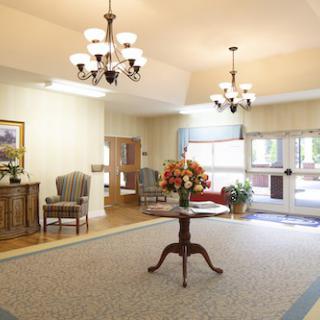 A bright and welcoming lobby area with chandeliers, elegant furniture, and a central table adorned with flowers.
