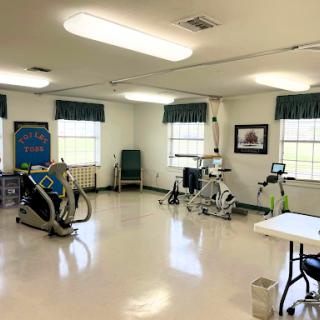 A bright and spacious physical therapy room equipped with various exercise machines and natural light from windows.