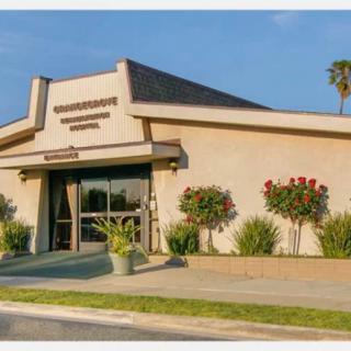 A beige building with an entrance surrounded by plants and flowers, featuring a palm tree in the background.