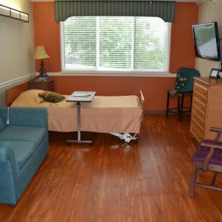 A spacious hospital room featuring a bed, a sofa, and a window with natural light.