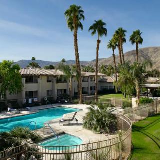 A scenic view of a resort featuring a swimming pool, surrounded by palm trees and mountains in the background.