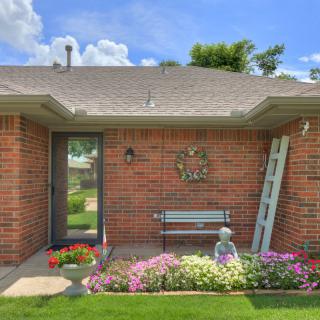 A cozy brick house with a small garden adorned with colorful flowers, featuring a bench and outdoor decor.