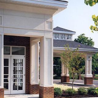 A modern building entrance featuring brickwork and columns surrounded by a landscaped courtyard.