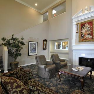 A spacious living room with high ceilings, featuring comfortable seating, a fireplace, and decorative artwork on the walls.