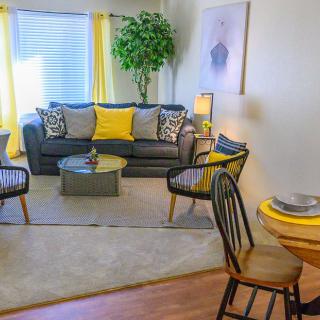 A cozy living room with a modern grey sofa and yellow accents, featuring armchairs and a central coffee table.