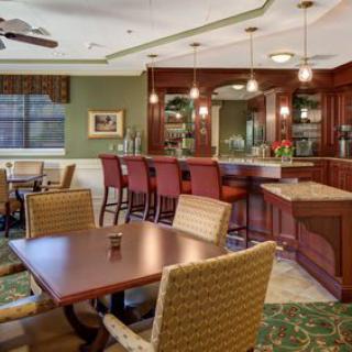 A cozy dining area with a bar, featuring tables and chairs, warm lighting, and a ceiling fan.