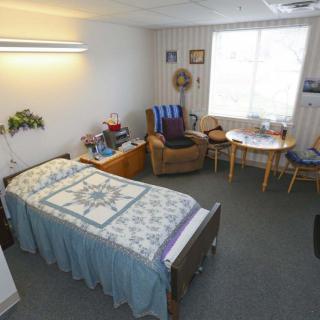 A cozy bedroom with a single bed, a small table set, and armchairs, illuminated by a large window.