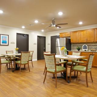 A modern dining area with multiple tables and chairs, adjacent to a kitchen with wooden cabinetry and stainless steel appliances.