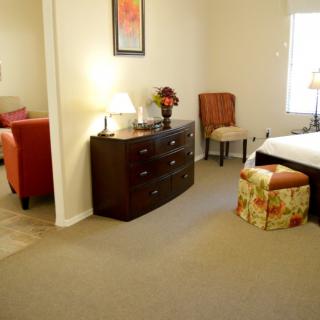 A cozy bedroom featuring a dresser with a lamp, a bed, and comfortable seating.