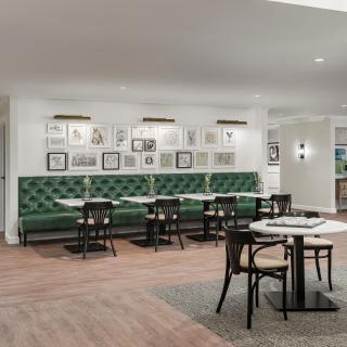 A modern restaurant interior featuring green upholstered seating, artistic wall decor, and stylish dining tables and chairs.