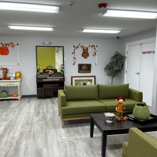 A cozy waiting room adorned with autumn-themed decorations and green sofas, featuring a coffee table and an indoor plant.
