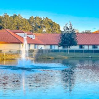 A serene view of a lake with a fountain, surrounded by residential buildings and lush greenery.