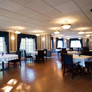 A spacious restaurant dining area with neatly arranged tables and chairs, well-lit by ceiling lights and natural light from the windows.