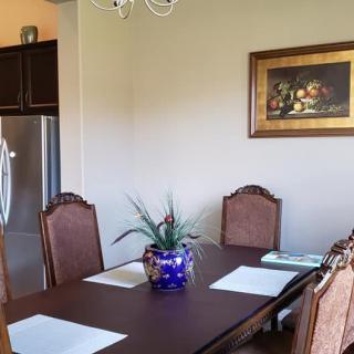 A cozy dining area with a wooden table, cushioned chairs, a plant centerpiece, and framed artwork on the wall.