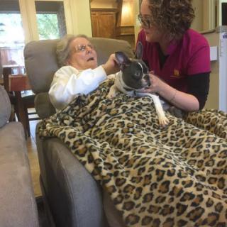 An elderly woman enjoying some quality time with a dog, assisted by a caregiver.